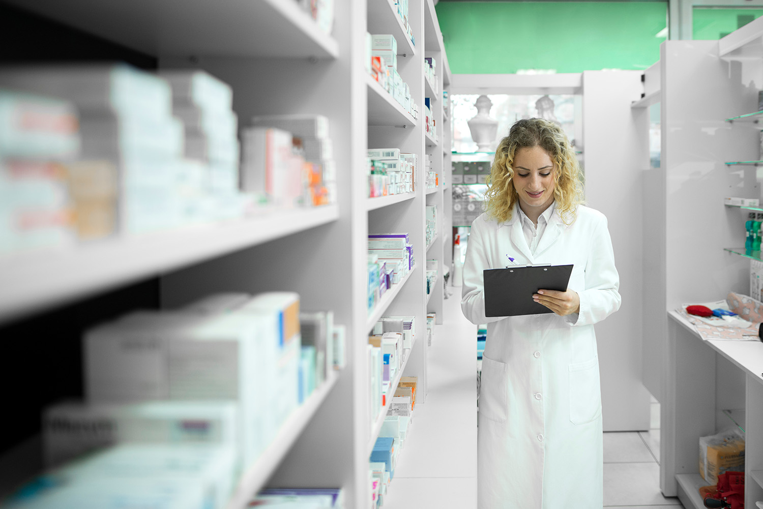 Pharmacist in white uniform walking by the shelf with medicines and checking inventory. Pharmaceutical industry.